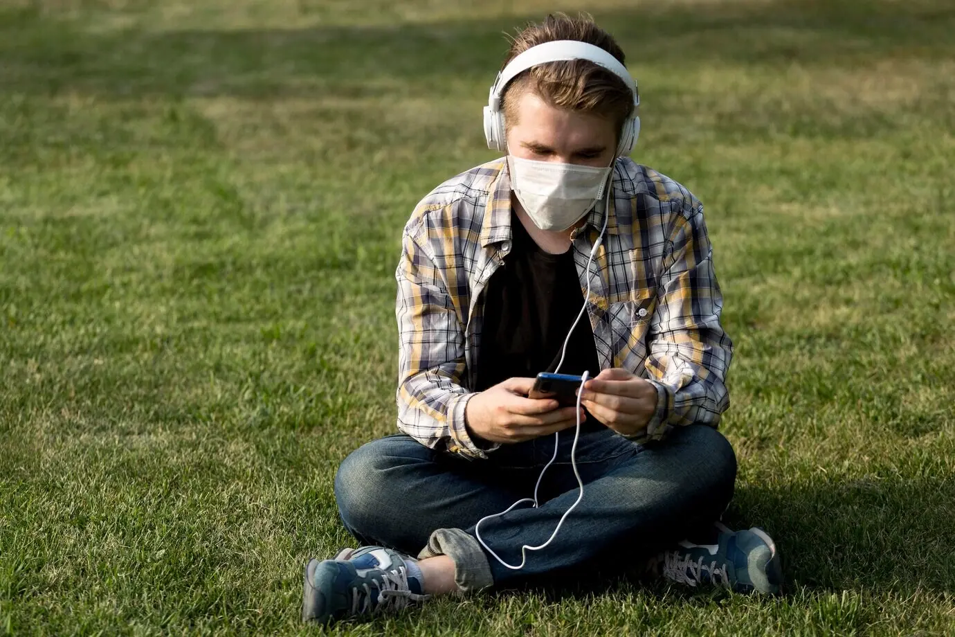 Молодой человек в маске на лице слушает музыку.